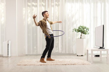 Young man spinning a hula hoop at home in front of tv