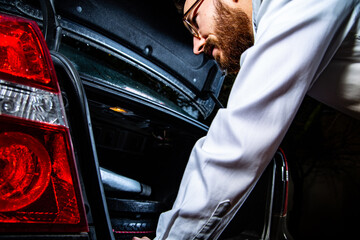 Young adult man looking into a car trunk.