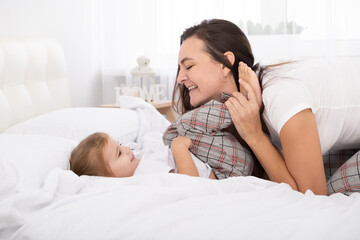 adult mother play with little active daughter in bed at home, having fun, activity with children.
