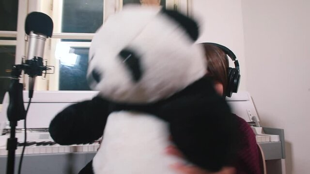 An inspired child in headphones is dancing with a panda sitting in the studio in front of a microphone. Throw a stuffed toy aside, dancing. Creative realisation of a teenager.