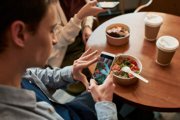 Close up of teenage guy with smartphone photographing his lunch at cafe