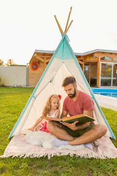 Father reading a story to his daughter while camping in the backyard