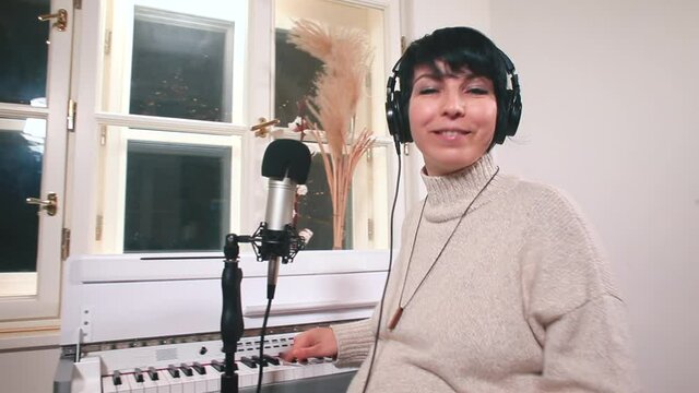 A pregnant woman in headphones is recording a song using a microphone and synthesizer. Creative realisation of a young mother on maternity leave.