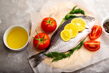 Fresh fish dorado fish on cutting board on white table with ingredients for cooking. Top view with copy space.
