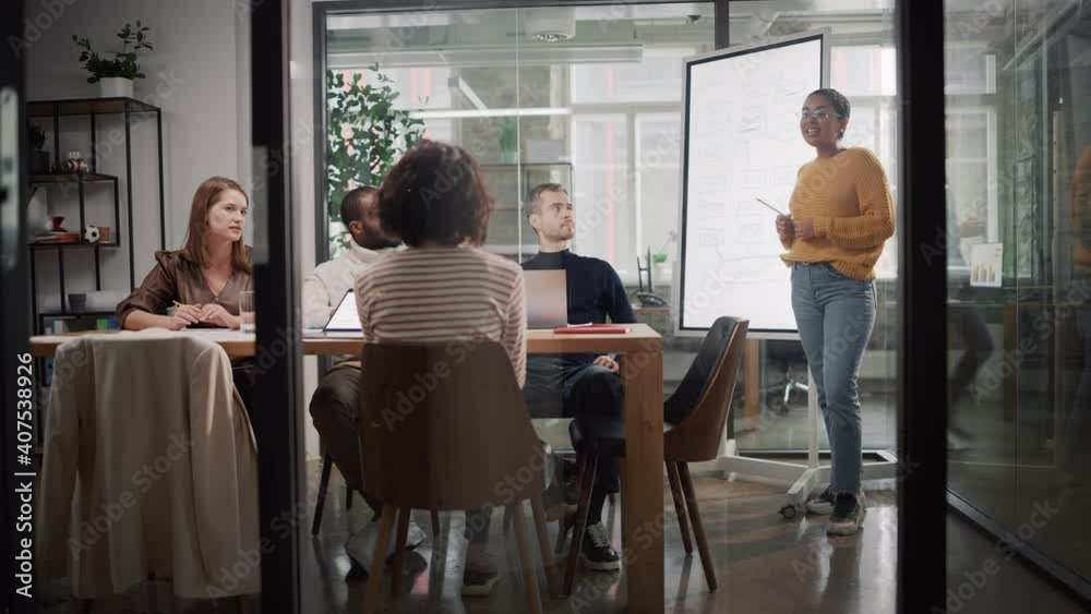Poster Project Manager Makes a Presentation for a Young Diverse Creative Team in Meeting Room in an Agency. Colleagues Sit Behind Conference Table and Discuss Business Development, User Interface and Design.