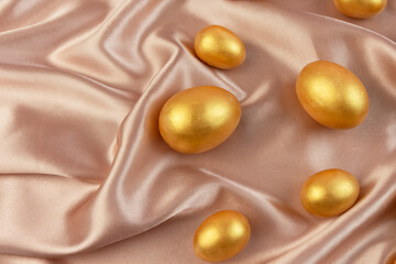 Golden decorative Easter eggs on a background of creamy shiny natural fabric. Soft texture concept. Champagne silk fabric.