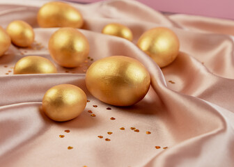 Golden decorative Easter eggs on a background of creamy shiny natural fabric. Soft texture concept. Champagne silk fabric.