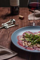 Delicious carpaccio on grey plate with a glass of red wine and corkscrew on wooden table