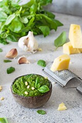 Green pesto in a bowl made from fresh basil leaves, pine nuts, parmesan, garlic and olive olia on a light background. Popular Italian dressing for salads, pasta and pizza.