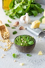 Green pesto in a bowl made from fresh basil leaves, pine nuts, parmesan, garlic and olive olia on a light background. Popular Italian dressing for salads, pasta and pizza.