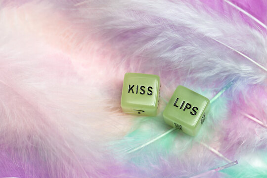 Two dice for erotic sexual game with the text Kiss lips for Valentines Day sex,romantic, sensual concept with pastel colored feather background