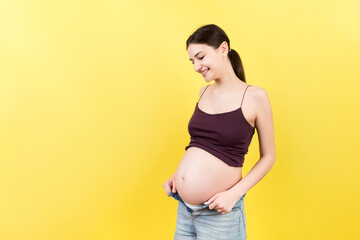 Happy pregnant woman in unzipped jeans showing her naked belly at colorful background with copy space. Baby expecting concept