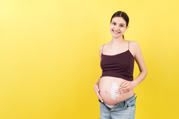 Close up of pregnant woman in opened jeans applying skin care cream on her belly to prevent stretch...