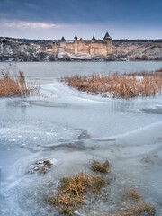 cold day on the river with view to the medieval castle behind frozen river in cloudy day