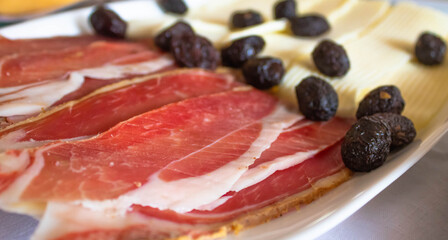 Traditional homemade Serbian ham in a plate, olives and cheese in the background