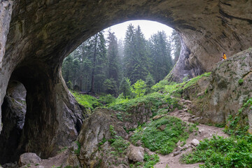 Bulgarian National park wonderful bridge and lady sitting on a rock with foggy mysterious recreation. Enormous cave and open hole. Geologic formation and tourist trip. Female alone on a trip