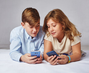 Fototapeta premium young girl and a boy playing in the phone, smiling and laughing. Children learn new technologies