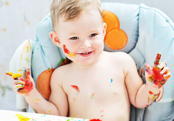 a small child boy smeared in colorful paint sits at the table.