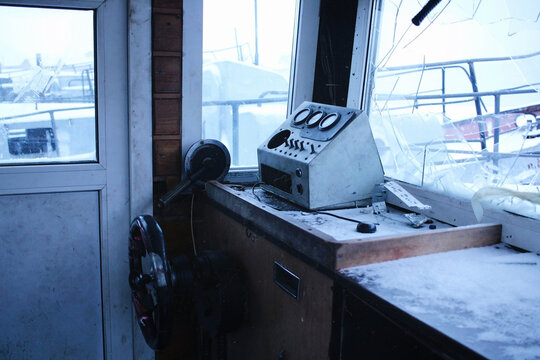 The wheelhouse of an abandoned ship. Broken ship window. Snow-covered dashboard