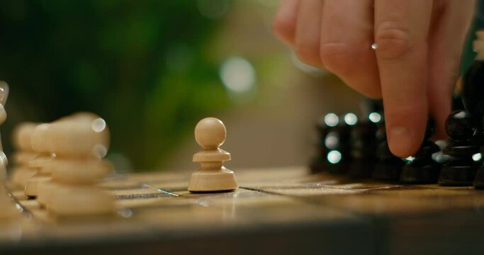 Close up to Wooden Chess Game with Gambit Opening. People Hands Playing Chess. Sport and Hobby Activities at Lockdown. White start to move pieces on chessboard with pawn. 4K Cinematic Macro Pan Shot