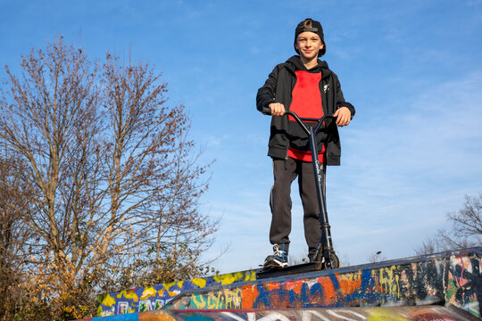 Ein netter und cooler Junge mit seinem schwarzen, trendigen Roller auf einem Spielplatz. Der Jugendliche ist sportbegeistert. Er f&auml;hrt gern mit seinem Scooter oder Fahrrad (Bike).