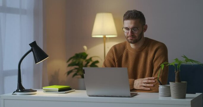 portrait of male participant of working video chat, man is nodding his head, viewing display of laptop, sitting in home