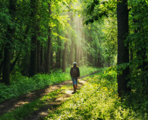 young woman walking along a forest trail with rays of sunlight shining through the leaves of the trees
