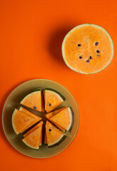 half of fresh ripe orange watermelon and slices at plate around orange background