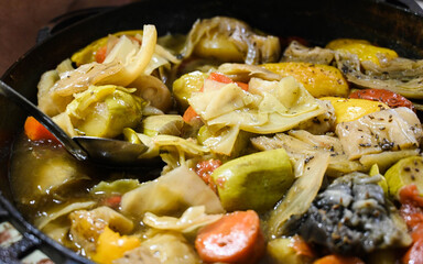 Huge spoon in freshly brewed thick delicious soup with vegetables  in a cauldron. Cabbage, carrots, zucchini, potatoes.