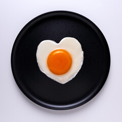 Heart shaped fried egg on a round black plate