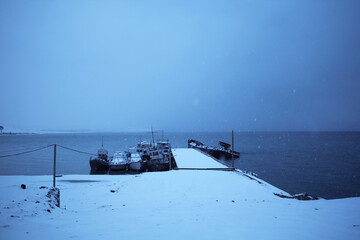 Port on Lake Baikal, Olkhon Island, Russia. Docks with abandoned and new ships. Snow covering the lake shore. Snowfall at dusk