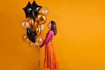 Dreamy girl holding party balloons. Positive female model posing after holiday event.