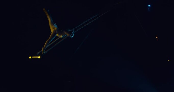 Young circus performer is swinging on a trapeze from the ceiling on the circus