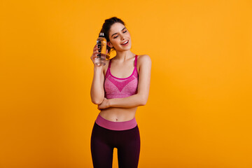 Pretty girl in good shape standing on yellow background. Sporty woman posing after training.