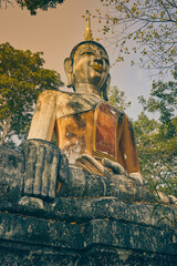 Phayao, Thailand - Dec 6, 2020: Portrait Front Right Meditation Buddha Statue in Green Forest and Blue Sky Background in Wat Analayo Temple in Vintage Tone