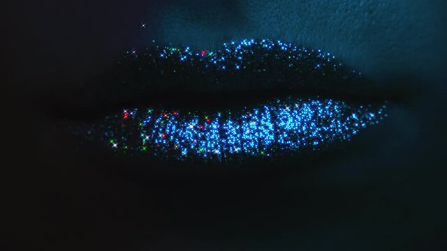 Fashion model with bright shiny sparkles on plump lips. Neon studio light. Macro view of woman with glamorous make-up. Nightlife, night club concept.