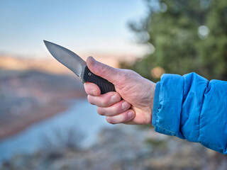 hand with an open pocket knife against mountain landscape - obrazy, fototapety, plakaty