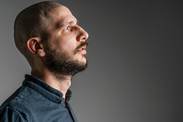 Fototapeta premium Side view close up portrait of adult caucasian man with beard and short hair looking up thoughtful with copy space - studio shot