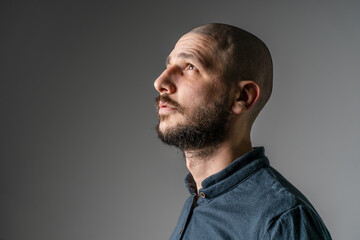 Side view close up portrait of adult caucasian man with beard and short hair looking up thoughtful with copy space - studio shot - Powered by Adobe