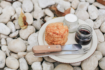 Delicious scones with Strawberry Jam and Clotted Cream on white rock in garden floor. Background and texture of white pebbles stone. English pastries concept.