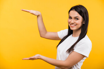 Smiling young caucasian woman in basic white t-shirt showing gesture with hands, standing on isolated orange background and looks at the camera. Copy space for text or advertising