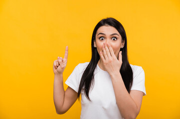 Shocked caucasian beautiful brunette woman covering her mouth with hand and surprised shows thumb up, standing against isolated orange background