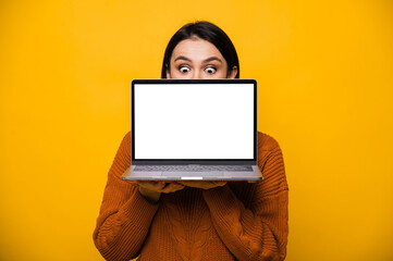 Portrait of a surprised shocked caucasian young woman, hiding behind blank white screen laptop,...