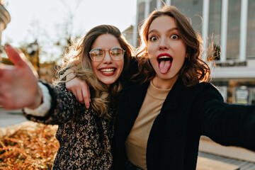Amazing woman in black coat making selfie. Graceful girls fooling around in autumn day.