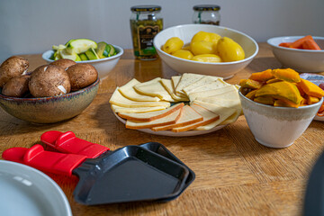 Detail photograph of a French raclette with all the typical ingredients, varieties of French cheeses, boiled potatoes, carrots, mushrooms, mushrooms, cucumbers and sausages, under natural light 