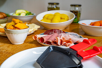 Detail photograph of a French raclette with all the typical ingredients, varieties of French cheeses, boiled potatoes, carrots, mushrooms, mushrooms, cucumbers and sausages, under natural light 