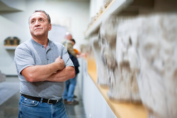 Positive cheerful smiling elderly man looking with interest at ancient sculptures in museum
