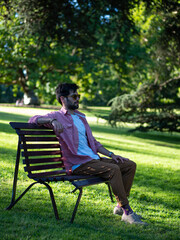 Fototapeta premium Young man sitting in a bank at the park using sun glasses