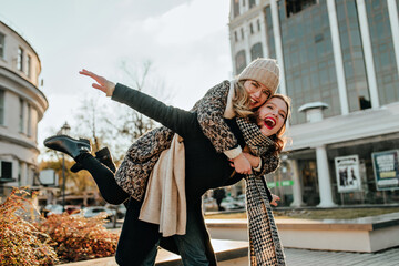 Woman in elegant coat spending october day with friend. Outdoor shot of two girls having fun in...