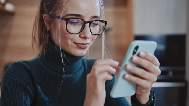 Portrait face young woman with glasses use phone smiling sitting near table. Message texting workplace smartphone browsing internet device. Slow motion